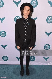a man wearing a hat and a suit is standing on a blue carpet at awards .