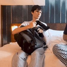 a man is sitting on a bed with a backpack on his lap