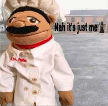 a puppet wearing a chef 's hat and coat is standing in front of a building .