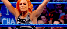 a woman is standing in a blue wrestling ring with her arms in the air .
