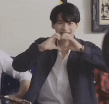 a man in a suit is making a heart shape with his hands while sitting in front of a guitar .