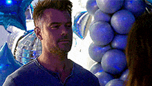 a man is standing in front of a bunch of blue balloons and looking at a woman .