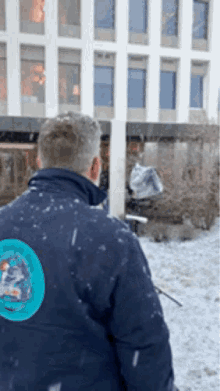a man wearing a blue jacket with a circle on the back is standing in the snow