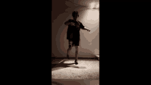 a person is squatting down in a dark room with a light on the wall behind them .
