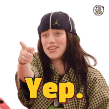 a woman wearing a hat and a plaid shirt is pointing at the camera and says yep