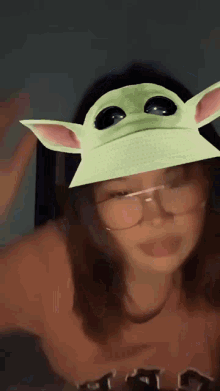 a girl wearing glasses and a green hat with a baby yoda face on it .