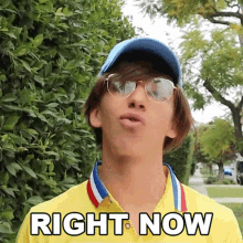 a young man wearing glasses and a yellow shirt is making a funny face and says right now .