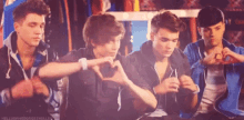 a group of young men are sitting next to each other making a heart shape with their hands .