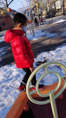 a child in a red jacket is playing on a playground in the snow