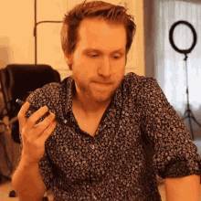 a man in a floral shirt is holding a cell phone in his right hand