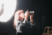 a woman with red hair is holding a camera in her hands