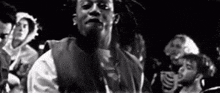 a black and white photo of a man with dreadlocks standing in front of a crowd of people .
