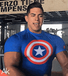 a man wearing a blue captain america shirt is standing in front of a sign that says " erzo tiene mpens "