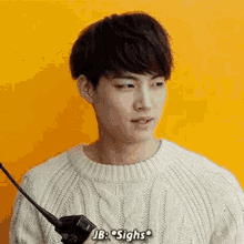 a young man wearing a white sweater is holding a walkie talkie .