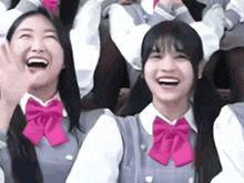 a group of girls in school uniforms with pink bows are laughing and waving .