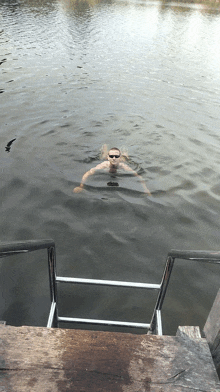 a man swimming in a body of water with a ladder in the foreground