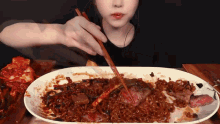 a woman is eating noodles with chopsticks from a plate