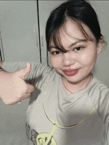 a woman giving a thumbs up while wearing a grey shirt with a yellow butterfly on it