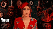 a woman in a red dress and red hat is standing in front of a wall of vases and plates .