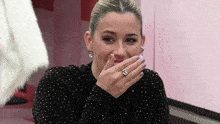 a woman is covering her mouth with her hand while wearing a ring .