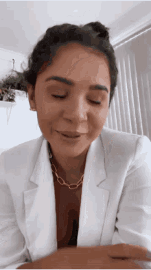 a woman wearing a white jacket and a gold chain necklace is smiling .
