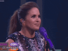 a woman in a sequined dress stands in front of a purple microphone with the time of 0.35