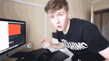 a man wearing a moschino shirt stands in front of a computer screen
