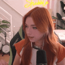 a woman with red hair is sitting in front of a microphone in front of a neon sign that says shubbly