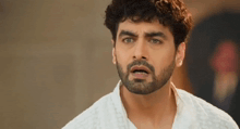a man with a beard and curly hair is wearing a white shirt and making a surprised face .
