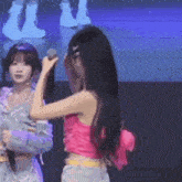 a woman in a pink crop top is holding a microphone while another woman looks on .