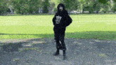 a person wearing a black hoodie and black pants is standing in front of a grassy field .