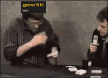two men are sitting at a table with a sign that says gperez1510 idolo on it
