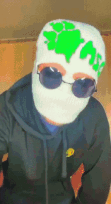 a person wearing a mask and sunglasses has a green sticker on their hat that says trash