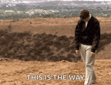 a man is walking on a dirt road with the words " this is the way " behind him