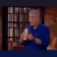 a man in a blue shirt is eating a banana in a kitchen .