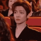 a man in a black shirt is sitting in a theatre looking at the camera .