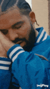 a man with braids and a beard is wearing a blue jacket with white stripes on the sleeves .