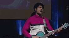 a man in a pink shirt is singing while holding a guitar