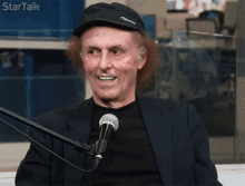 a man wearing a black hat and a black jacket is smiling in front of a microphone with the words startalk written on the top