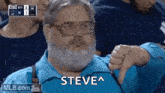 a man with a beard and glasses is giving a thumbs down sign while watching a baseball game .
