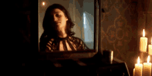 a woman is looking at her reflection in a mirror in a dark room with candles .
