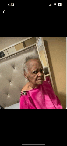 an elderly woman is sitting on a bed wearing a pink towel .