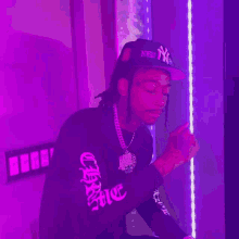 a man wearing a new york yankees hat stands in front of a purple wall