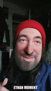 a man with a beard wearing a red hat with the words ethan moment written below him