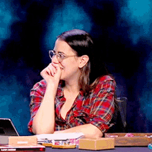 a woman wearing glasses sits at a table with a box that says ' a ' on it in front of her