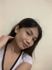 a woman wearing a white shirt and a heart necklace looks at the camera