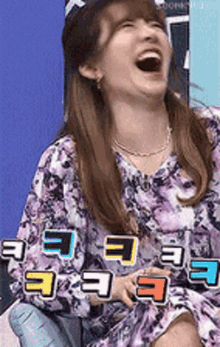 a woman in a purple floral dress is laughing with the letter e on her shirt
