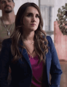 a woman wearing a blue jacket and a necklace with a ring on it