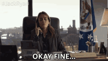 a woman sitting at a desk talking on a cell phone and says okay fine