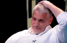 a man with gray hair and a beard is holding his head with his hand .